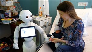 New recruit *Pepper* the robot, a humanoid robot designed to welcome and take care of visitors and patients, holds the hand of a new born baby next to his mother at AZ Damiaan hospital in Ostend, Belgium June 16, 2016.