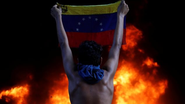 A protester holds a national flag as a bank branch, housed in the magistracy of the Supreme Court of Justice, burns during a rally against Venezuela’s President Nicolas Maduro, in Caracas, Venezuela June 12, 2017.