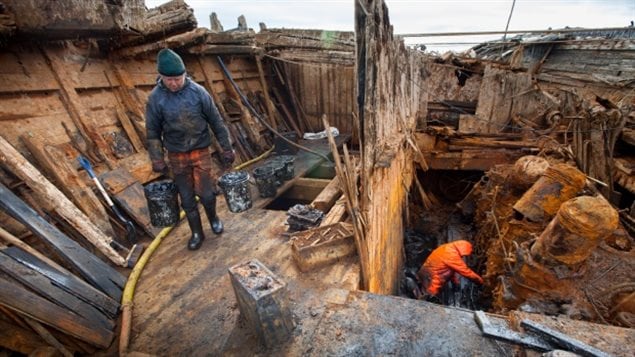 Members of the Maud Returns Home group, Stig Pettersen carries a heavy load of mud from the Maud while Terje Morved digs out the engine. One can see the huge pistons exposed. Tons of mud had to be removed much of it by hand.