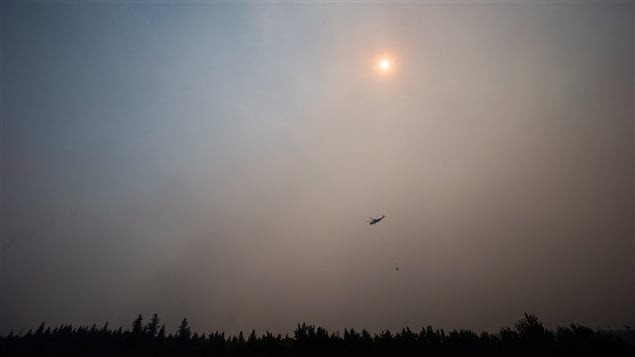 Smoke obscures the sun as a helicopter carrying a bucket battles the Gustafsen wildfire near 100 Mile House, B.C., on Saturday July 8, 2017. More than 180 fires were burning, many considered out of control, as the B.C. government declared a provincewide state of emergency to co-ordinate the crisis response. 