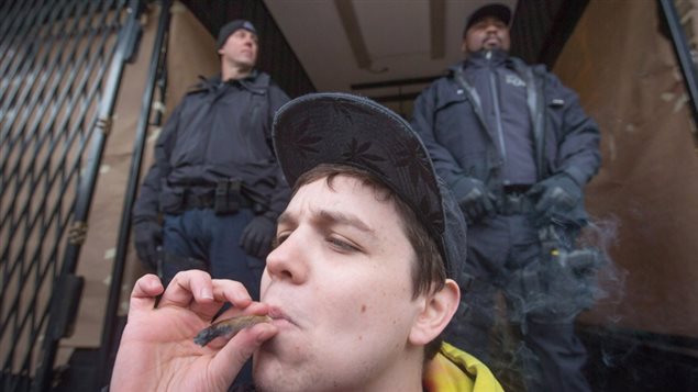A young man smokes a joint as police officers stand outside the Cannabis Culture shop during a police raid in Vancouver, B.C. on Thursday March 9, 2017.