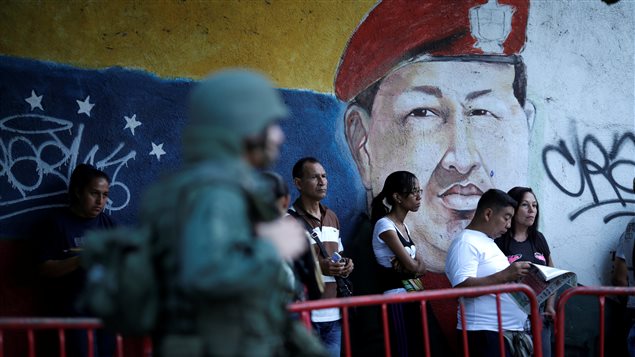 People wait in line next to an image of the late Venezuelan President Hugo Chavez before voting during the Constituent Assembly election in Caracas, Venezuela July 30, 2017.