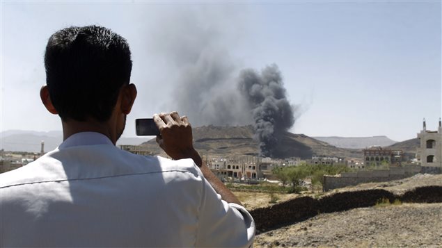 A man films with a mobile phone as smoke rises after explosions were set off at the army’s First Armoured Division headquarters in Sanaa October 18, 2012.