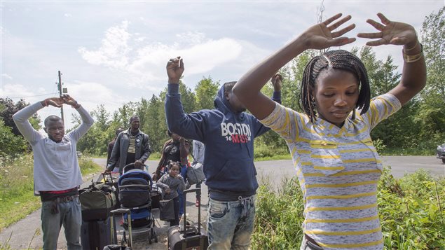 A group of asylum seekers raise their hands as they approach RCMP officers while crossing the Canadian border Friday, August 4, 2017 from Champlain, N.Y.