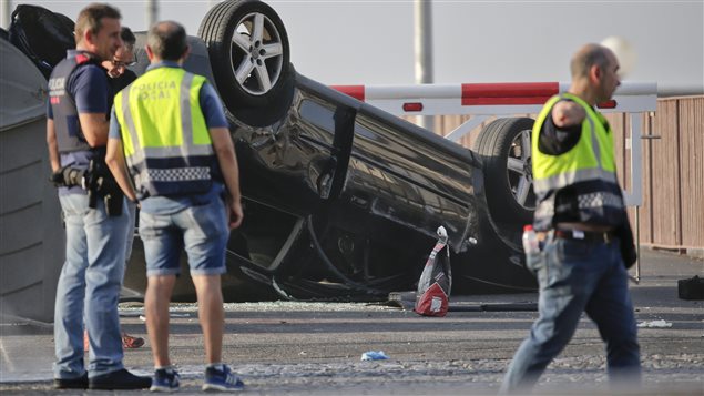 Police officers walk near an overturned car onto a platform at the spot where terrorists were intercepted by police in Cambrils, Spain, Friday, Aug. 18, 2017. 