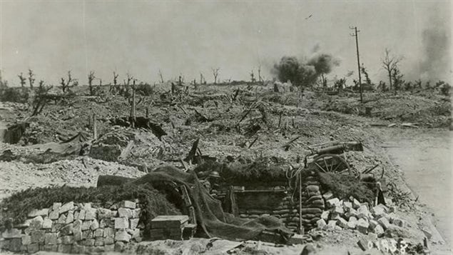 A German shell bursts in a blasted landscape near a Canadian gun pit at Hill 70. The howitzer has a net draped over it, presumably to conceal it from possible enemy spotter planes. Part of the wheel and gun trail can be seen