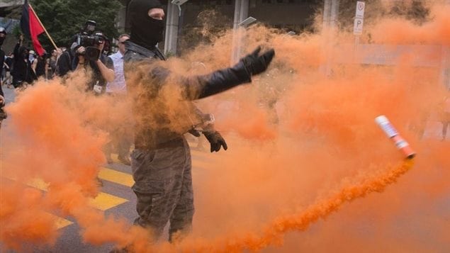 An anti-racism protestor throws a smoke flare into the police lines in Quebec City on Sunday.