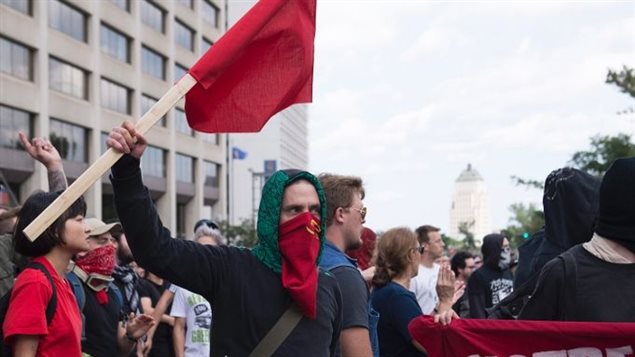 A man with a communist face-mask and holding a communist flagis shown among the group of anti-racist demonstrators, in Quebec City on Sunday, Aug. 20, 2017. 