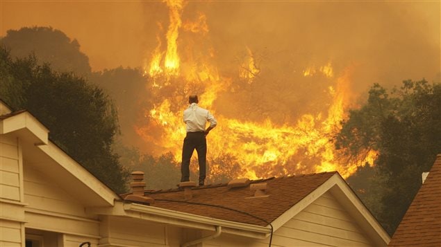 Un homme regarde le feu s’approcher de sa maison. Les feux de forêt plus fréquents sont l’un des phénomènes que l’on associe au rechauffement climatique.