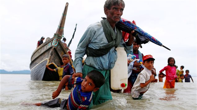 A Rohingya refugee man pulls a child as they walk to the shore after crossing the Bangladesh-Myanmar border by boat through the Bay of Bengal in Shah Porir Dwip, Bangladesh, September 10, 2017.