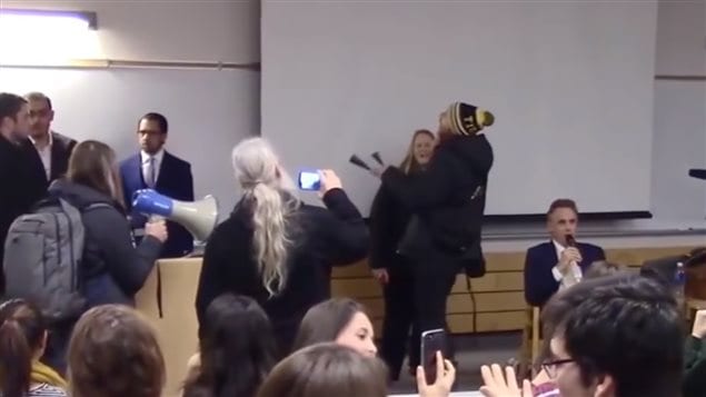 March 2017: McMaster University *debate*. Renowned University of Toronto professor Jordan Peterson (sitting right) attempts to discuss freedom of expression issues logically. Controversial for his position against forced use of gender-neutral pronouns, the university had permitted the event to go on in spite of requests by some to cancel it, but it was shut down anyway by a group of protesters banging cowbells, bellowing through loudspeakers and chanting obscenities, an example of minority groups shutting down free speech on campus.