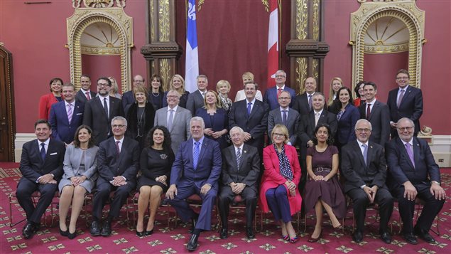 صورة للحكومة الكيبيكية الجديدة أُخذت اليوم في مبنى الجمعية الوطنية في كيبيك بعد التعديل الذي أعلنه رئيسها فيليب كويار (الخامس من اليسار في الصف الأول جلوساً).