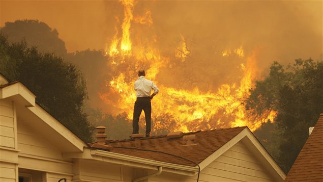Un homme regarde le feu s’approcher de sa maison. Les feux de forêt plus fréquents sont l’un des phénomènes que l’on associe au rechauffement climatique.Photo Credit: David McNew/Getty Images