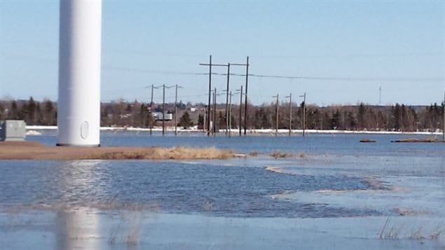 A wind turbine and power poles are surrounded by floodwater on the Tantramar Marsh