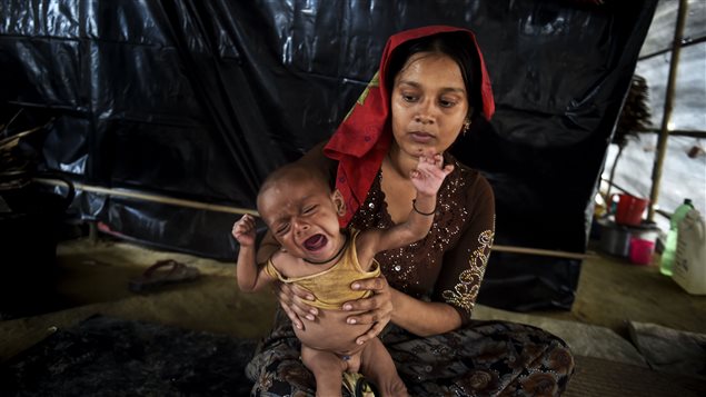 This photograph taken on November 17, 2017 shows a six-month-old Rohingya refugee boy named Mohammad Wahid, who is suffering from malnutrition, sitting on his mothers lap inside a makeshift shelter at Thankhsli camp in the Bangladeshi district of Ukhia.