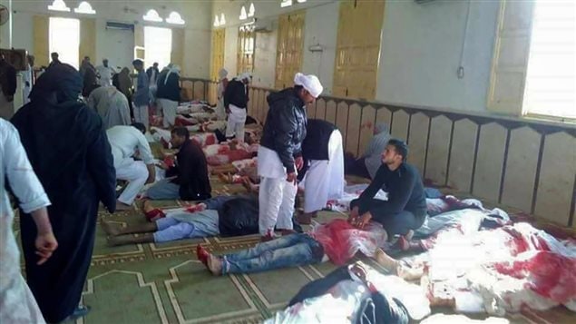 Egyptians walk past bodies following a gun and bombing attack at the Rawda mosque, roughly 40 kilometres west of the North Sinai capital of El-Arish, on November 24, 2017. A bomb explosion ripped through the mosque before gunmen opened fire on the worshippers gathered for weekly Friday prayers, officials said.