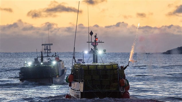 A crew member sets off fireworks as boats leave a Nova Scotia harbour for the start of lobster fishing season off eastern Canada.