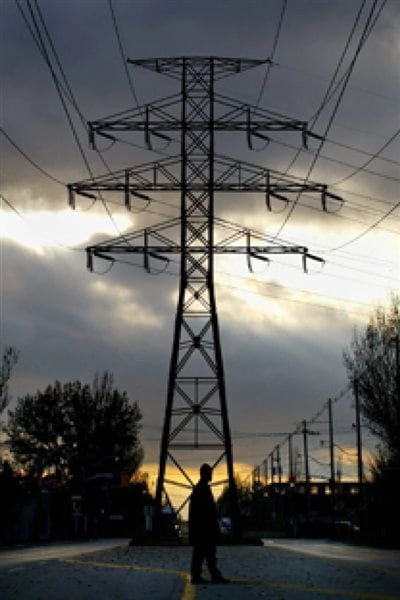 A pedestrian stands under a hydro tower in downtown Toronto in November 2002. Electricity costs in Ontario have risen dramatically in spite of vast amounts of surplus