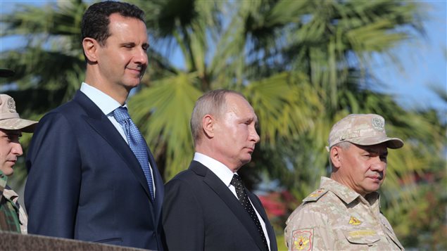 الرئيس الروسي فلاديمير بوتين محاطاً بالرئيس السوري بشّار الأسد عن يمينه وبوزير الدفاع الروسي سيرغي شويغو عن يساره، يوم الاثنين في قاعدة حميْميم الجوية الروسية في محافظة اللاذقية السورية