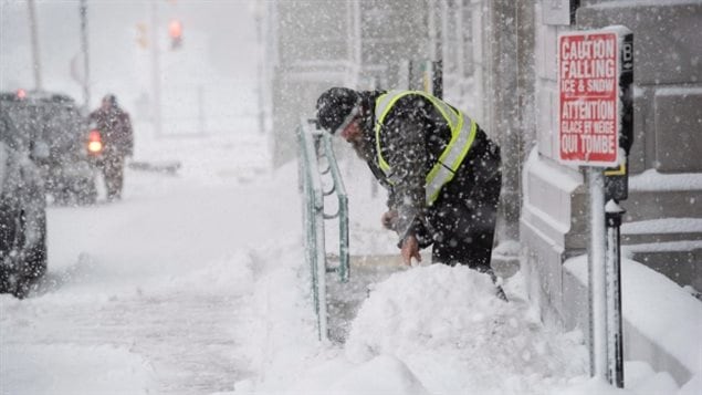 رجل يزيل الثلوج يوم الخميس من أمام مدخل أحد الأبنية الفدرالية في مدينة مونكتون في مقاطعة نيو برونزويك (نوفو برونزويك) الكندية المطلة على الأطلسي 