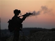 photo à la pénombre: ombre d'un soldat pointant son arme vers l'horizon : de la fumée quitte son canon.