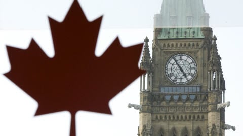 Le Parlement canadien, vu derrière une fenêtre sur laquelle a été apposée une feuille d'érable.