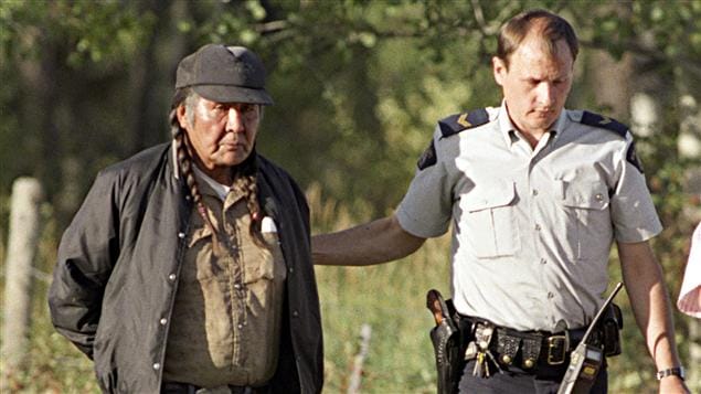John Ignace, surnommé Wolverine, un des Autochtones ayant occupé un terrain au bord du lac Gustafsen, en Colombie-Britannique, est escorté par un agent de la Gendarmerie royale le 17 septembre 1995.