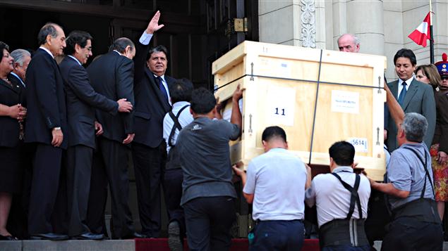 Le président du Pérou salue les journalistes tandis qu'on transporte la première caisse de pièces archéologiques restitutées par l'Université de Yale.