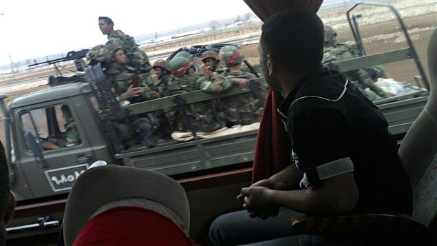 Sur cette photo prise avec un téléphone cellulaire, un Syrien assis dans un autobus observe un camion transportant des militaires près de Homs.