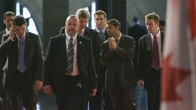 Stephen Harper discute avec son ancien directeur des communications Dimitri Soudas, entouré de gardes de sécurité, en 2008, au parlement.