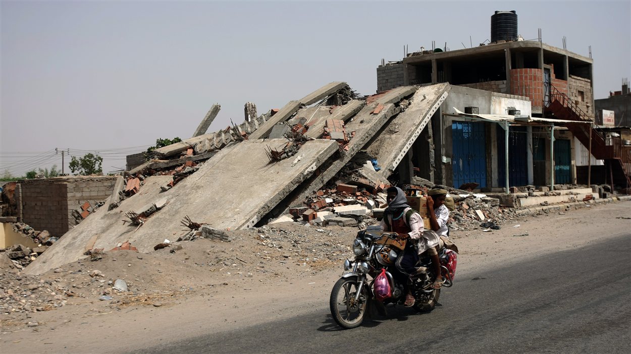 Des hommes circulent à moto devant un bâtiment effondré après l’offensive de l’armée à Jaar.