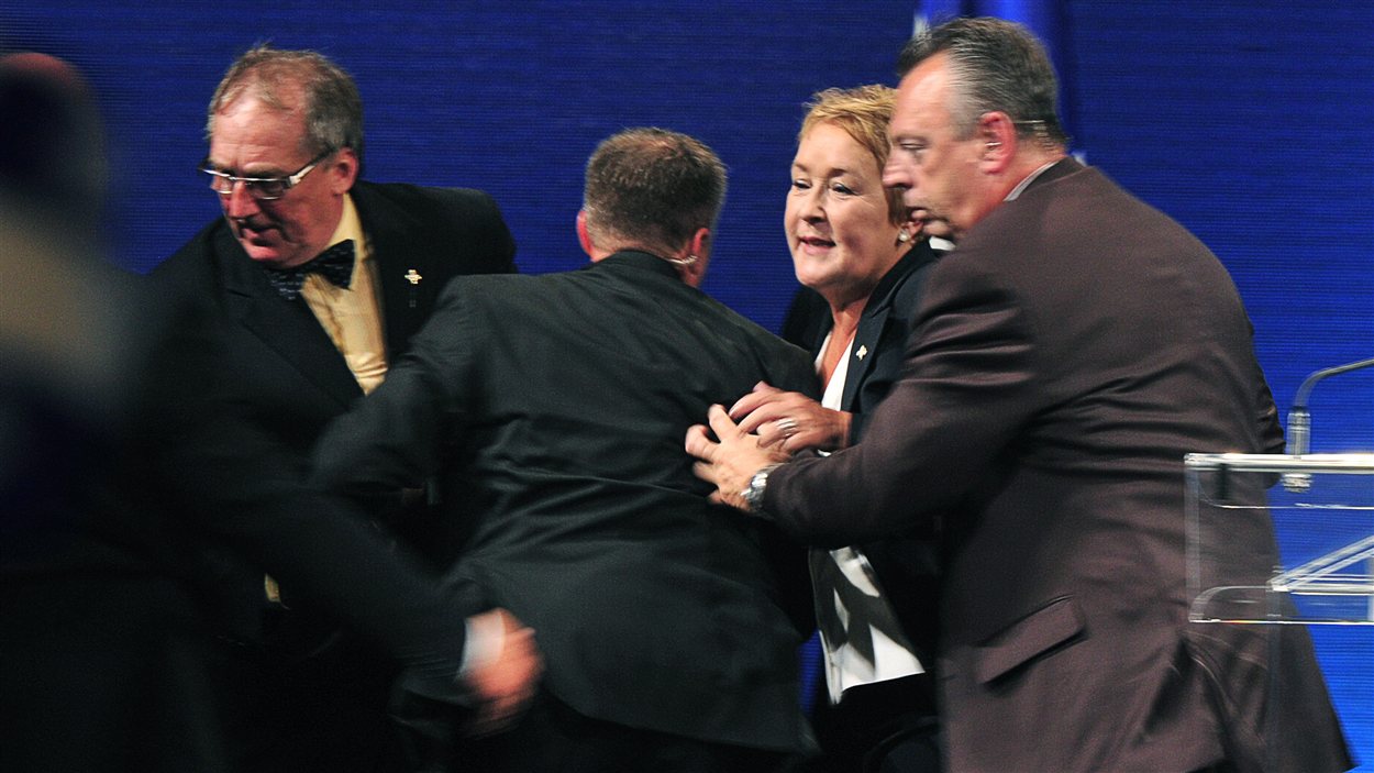 La chef du Parti québécois, Pauline Marois, est poussée hors de la scène par ses gardes du corps.