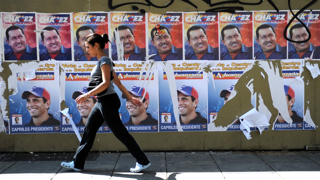 Une Vénézuélienne en train de marche devant des affiches du président sortant Hugo Chavez et du candidat de l'opposition Henrique Capriles, à Caracas.