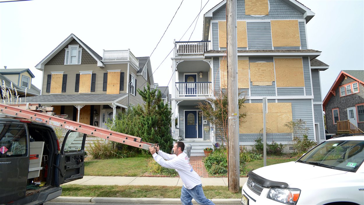 À Cape May, aux États-Unis, un homme range une échelle après avoir installé des panneaux sur les fenêtres et les portes de sa demeure pour la protéger de l’ouragan Sandy.