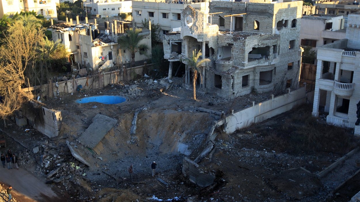 Deux hommes examinent le cratère laissé par une bombe israélienne dans la bande de Gaza.