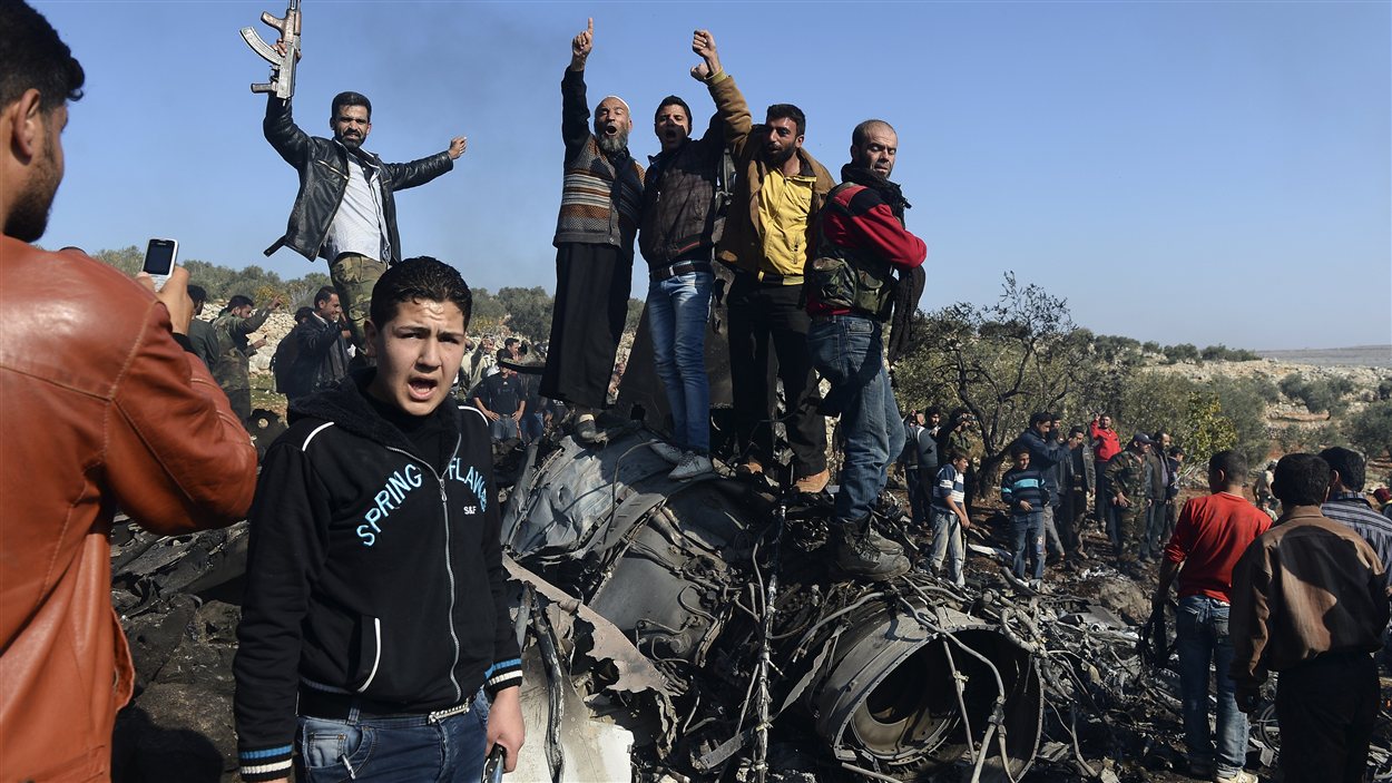 Des rebelles et des civils syriens célèbrent leur succès sur la carcasse de l'avion de chasse abatu.