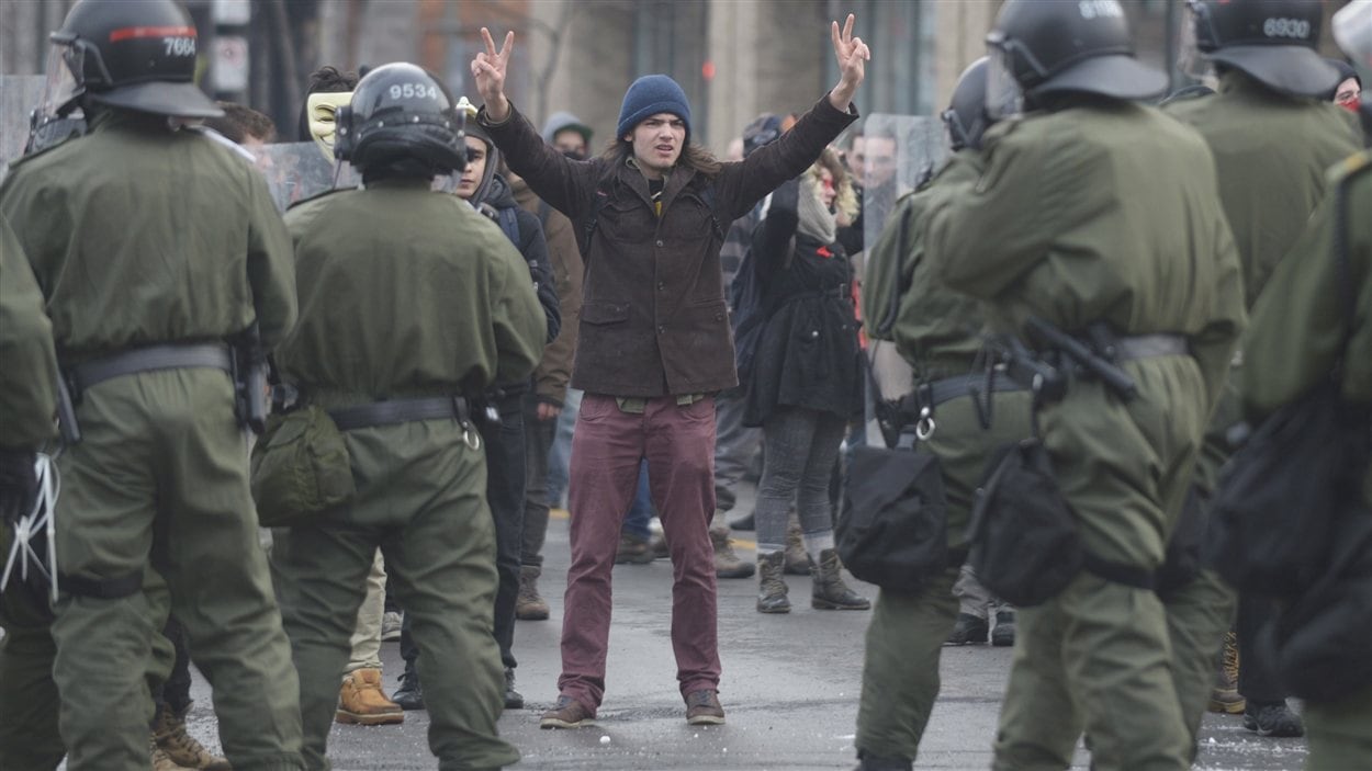 Un manifestant écarte victorieusement ses doigts en face de policiers de la SQ.