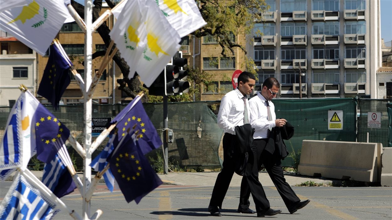 Des Chypriotes marchent près de drapeaux de Chypre, de l'Union européenne et de la Grèce, à Nicosie.