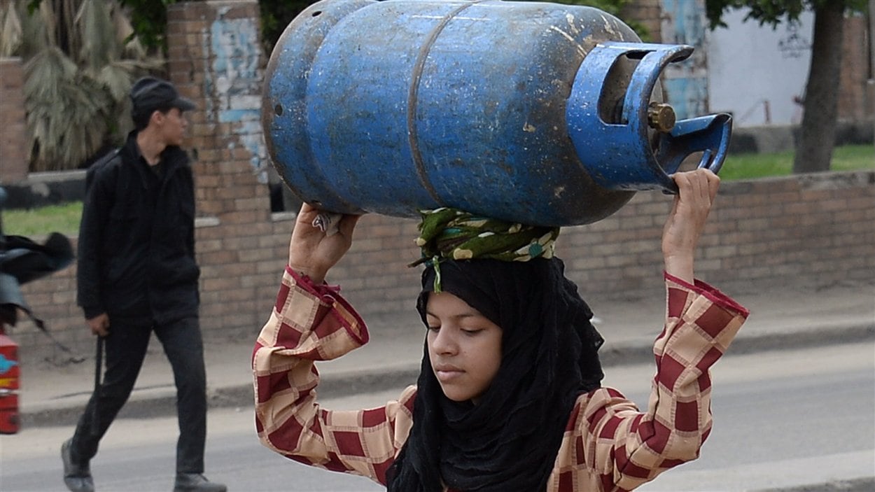 Une jeune femme transporte une bonbonne de gaz vide dans les rues du Caire