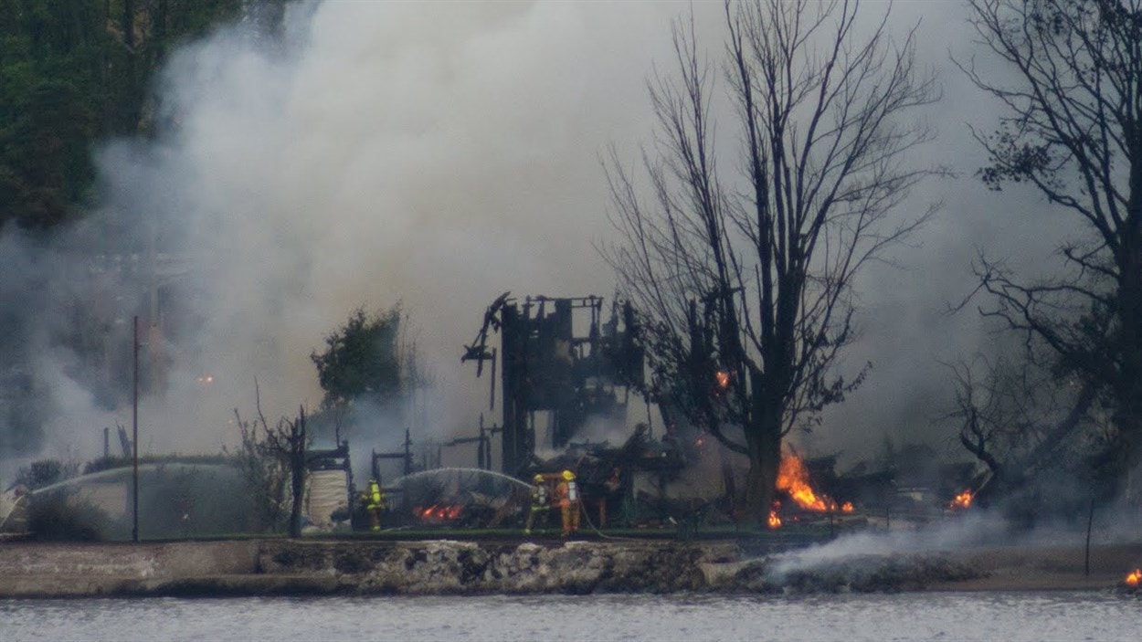 Des pompiers éteignent les décombres d'un bâtiment rasé par les flammes en bordure du lac Mégantic.