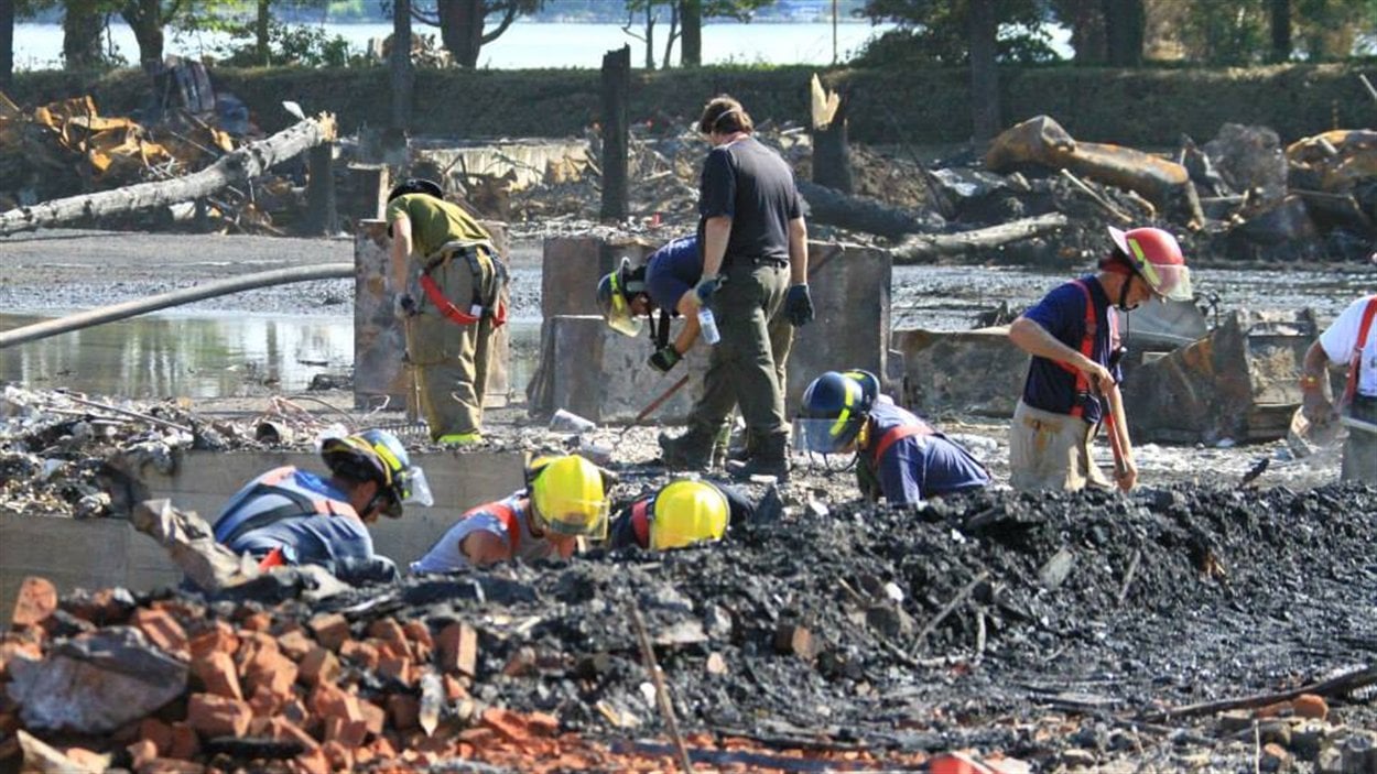 Des pompiers fouillent dans les restes de la locomotive qui a explosé au centre-ville de Lac-Mégantic.