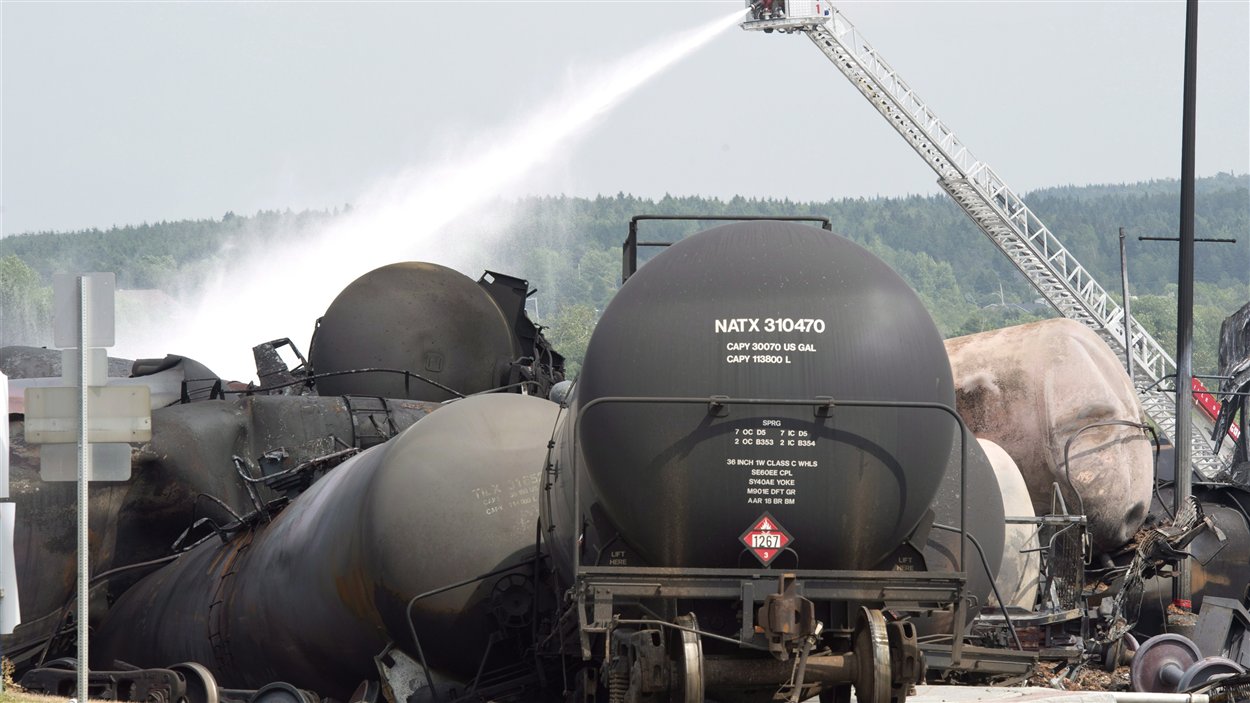Des pompiers arrosent l'un des nombreux wagons qui a pris en feu à Lac-Mégantic.