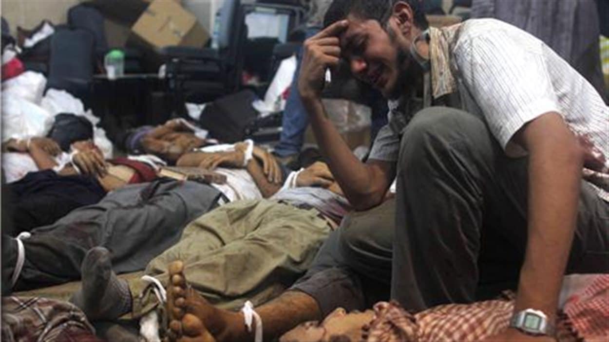 Un homme pleure parmi les cadavres étendus au sol dans une morgue de fortune, place Rabia al-Adawiya.