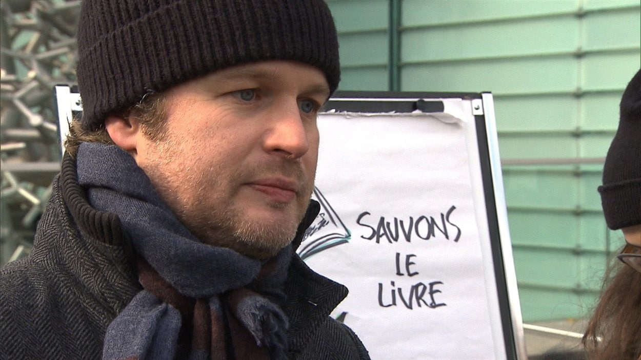 L'auteur et éditeur Tristan Malavoy-Racine devant l'affiche « Sauvons les livres » dessinée par l'illustrateur Jacques Goldstyn.