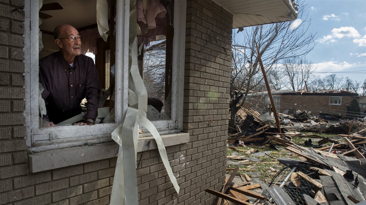 Un résident observe un décor d’après-guerre depuis la fenêtre de sa maison détruite.