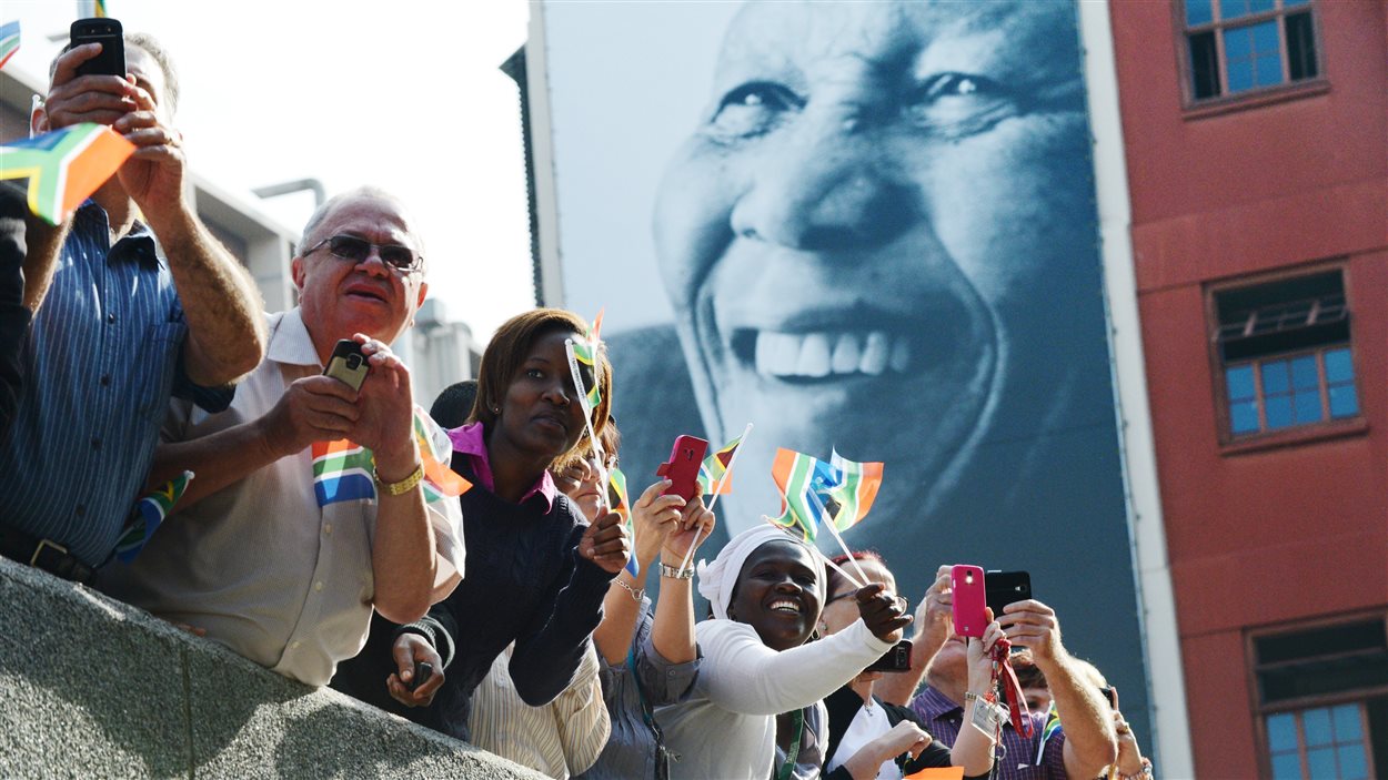 Des Sud-Africains regardent le cortège funèbre transportant le corps de Mandela vers le siège du gouvernement et de la présidence à Pretoria, la capitale.