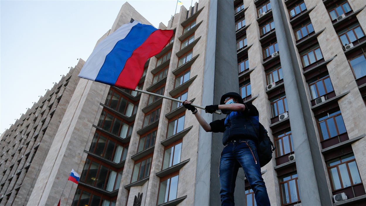 Un militant masqué agite un drapeau russe en face du bâtiment de l'administration régionale de Donetsk, en Ukraine.