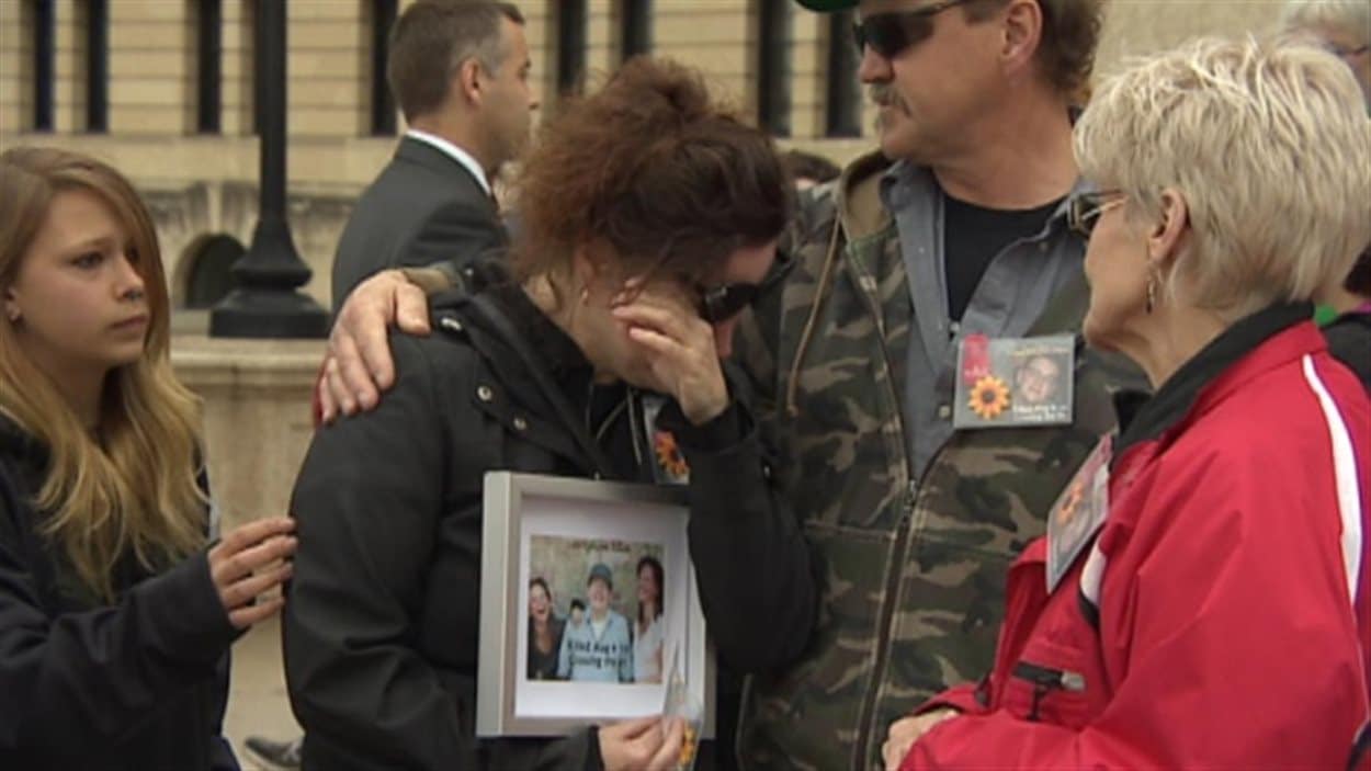Durant une manifestation devant le palais législatif de la Saskatchewan le 6 mai 2014, une femme essuie ses larmes en tenant la photo d'un proche mort dans un accident sur le tronçon de la transcanadienne entre Regina et Balgonie.