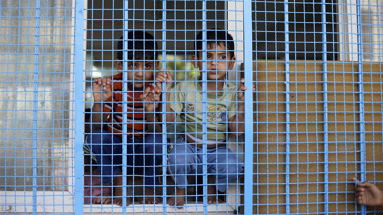Des enfants palestiniens ayant fui leur maison regardent à travers le grillage d'une école où ils se sont réfugiés à Rafah