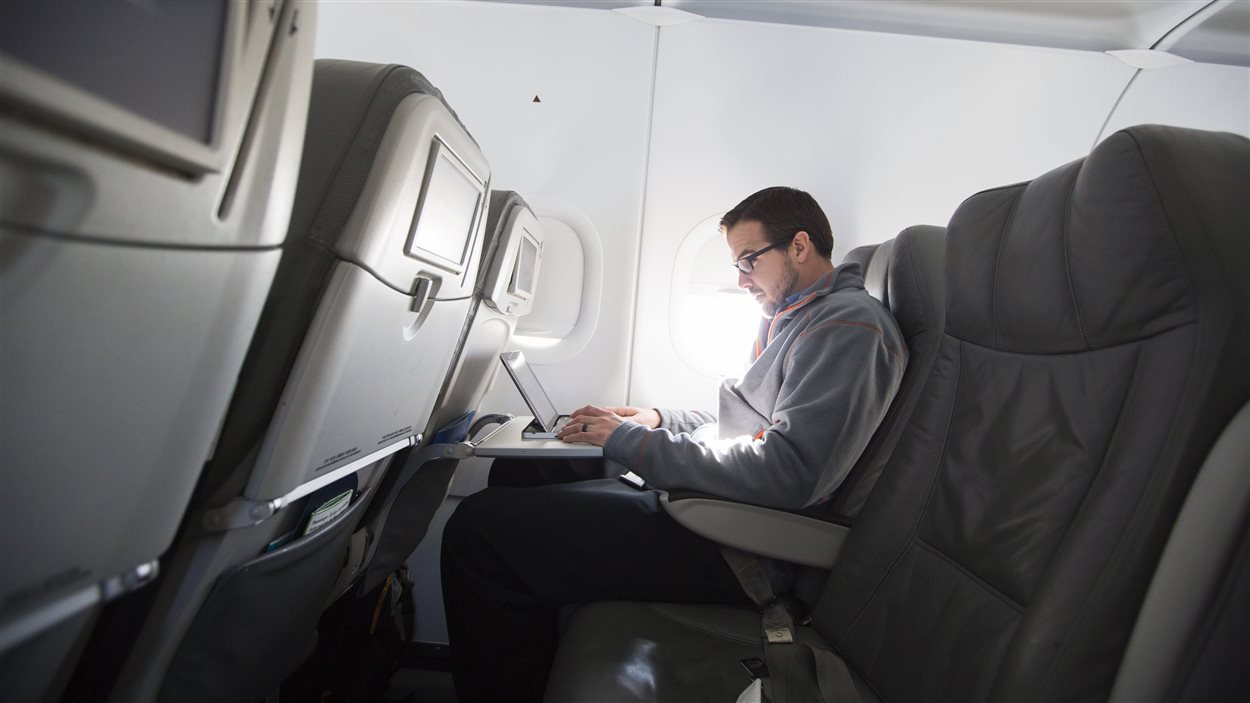 Un homme utilise son ordinateur à bord d'un avion.
